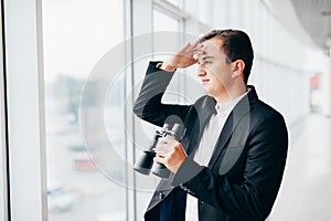 Business man looking with binoculars on competitors over panoramic windows