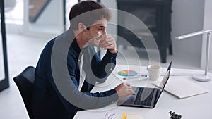 Business man looking documents on laptop. Smiling guy analyzing financial charts