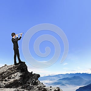 Business man looks through telescope on mountain