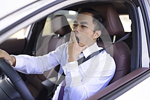 Business man looks tired yawning while driving the car