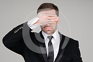 Business man making the see no evil gesture. Businessman covering his eyes with his hand
