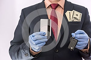 Business man in medical gloves holding credit card and car key, with money in poket, epidemic covi19 photo