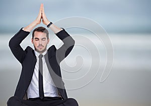 Business man meditating against blurry beach