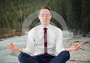 Business man meditating against river