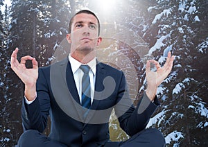 Business man meditating against snowy trees with flare
