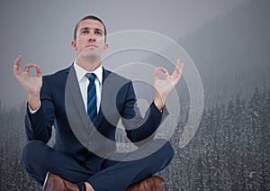 Business man meditating against trees and grey sky