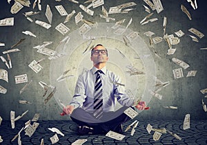 Mature business man meditating under money rain