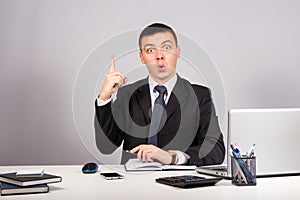 Business man at office holding finger up: idea or warning on gray background
