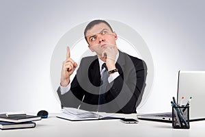 Business man at office holding finger up: idea or warning on gray background