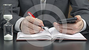 Business man in the office is working with a mobile phone on the background of an hourglass. business and successful goal