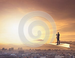 Business man on paper plane spying by binocular to urban scene