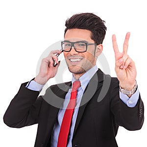 Business man on phone shows victory sign