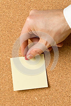 Business man pinning empty yellow sticky paper memo note on cork board