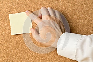 Business man pinning empty yellow sticky paper memo note on cork board