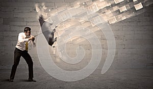 Business man protecting with umbrella against wind of papers