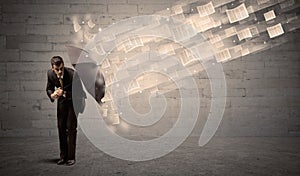 Business man protecting with umbrella against wind of papers