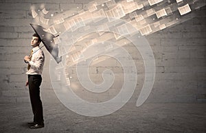 Business man protecting with umbrella against wind of papers