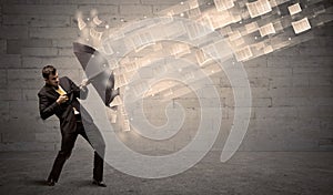 Business man protecting with umbrella against wind of papers