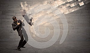 Business man protecting with umbrella against wind of papers