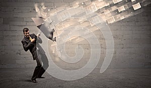 Business man protecting with umbrella against wind of papers