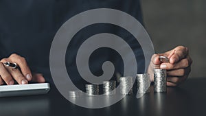 Business man putting a coin on a pile of coins. Placing coins in a row from low to high is comparable to saving money to grow more