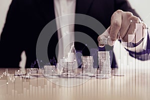 Business man putting coin on pile of money on table with financial graph background