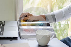 Business man is reading a book with a laptop by the window on the desk in staying at home.