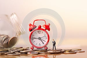 Business man and red alarm clock on stack of coins in concept of savings and money growing or energy save.