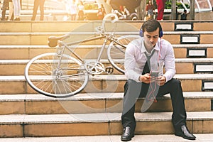 Business man relaxing listening to music with his bicycle on