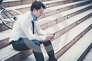 Business man relaxing listening to music with his bicycle on the side