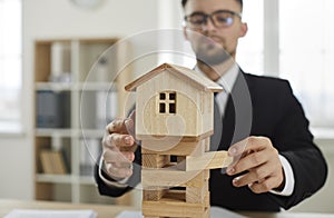 Business man removes blocks from under toy house as concept of unstable real estate market