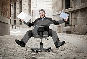 Business man rolling downhill on chair with computer and tablet