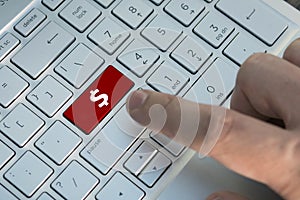 Business man's hand pushing on keyboard with abstract dollar sign. A male finger presses a color button on a gray silver keyboard