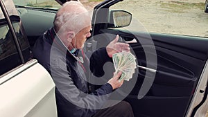 The business man sat down on the doorstep of the car and count the money.