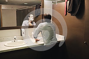 Business Man Shaving In Office Bathroom After Early Morning Commute