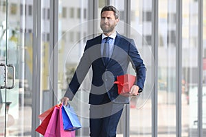 Business man shopping in a shopping center. Happy businessman in suit holding paperbags. Shopaholic man walking on