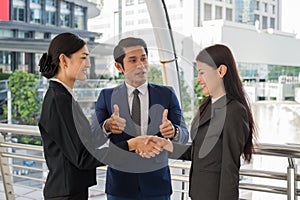 Business man show thumb up and two business woman shaking hands for demonstrating their agreement to sign agreement or contract