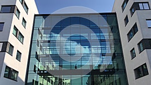 Business man in silhouette walking through a glass hallway in modern office building with reflections of blue sky and white clouds