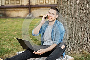 Business man sit on lawn work outdoors on computer and talking on phone in a park. student with laptop sit in grass