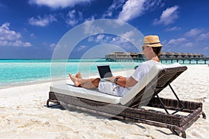 Business man sits on a tropical beach with his laptop and works