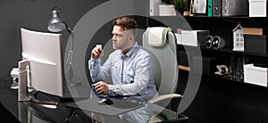 Business man sitting in office at computer Desk and holding his mouth shackle of glasses