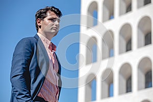 Business man standing in front of a building. Wearing a shirt and formal suit