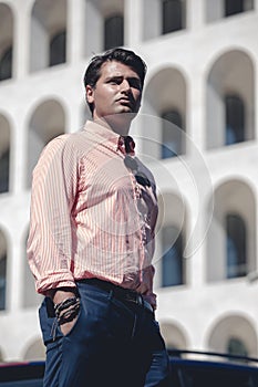 Business man standing in front of a building. Wearing a shirt and formal suit. Hands in the pocket