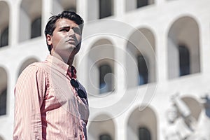 Business man standing in front of a building. Wearing a shirt. Look into the distance