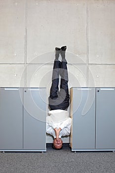 Business man standing on his head between cabinets in office