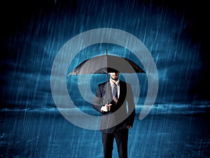 Business man standing in rain with an umbrella