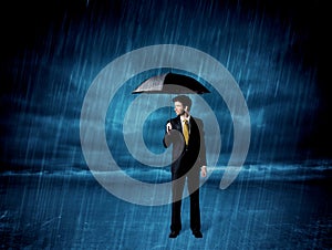 Business man standing in rain with an umbrella