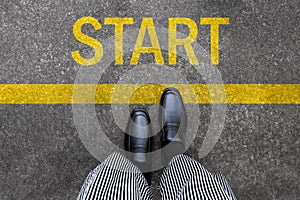 Business man standing on street background with word new start written. Pair of feet and black shoes on tarmac road with yellow