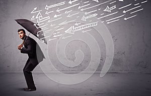 Business man standing with umbrella and drawn arrows hitting him