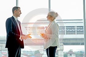 Business man stands and discuss with young beautiful woman in the room with glass windows